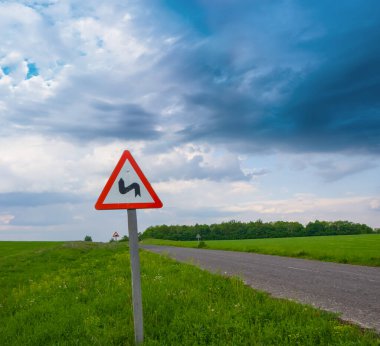 Yeşil tarlalar arasında yol tabelasıyla asfalt yola dön