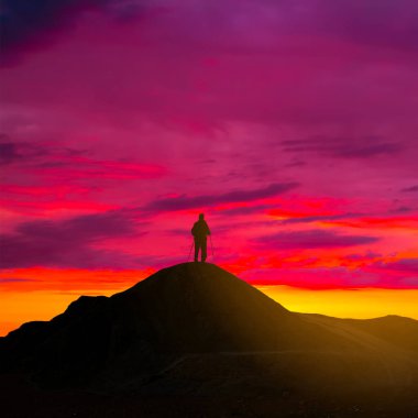 Yürüyüşçü silueti dağın tepesinde kalır dramatik günbatımında, doğal seyahat arka planında