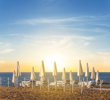 Güneşin batışında şemsiyesi olan kumlu deniz plajı, yaz tatili arka planı. 