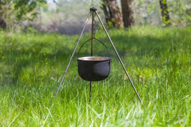lagre touristic cauldron on a tripod among forest glade with green grass, nice camping background, touristic travel scene