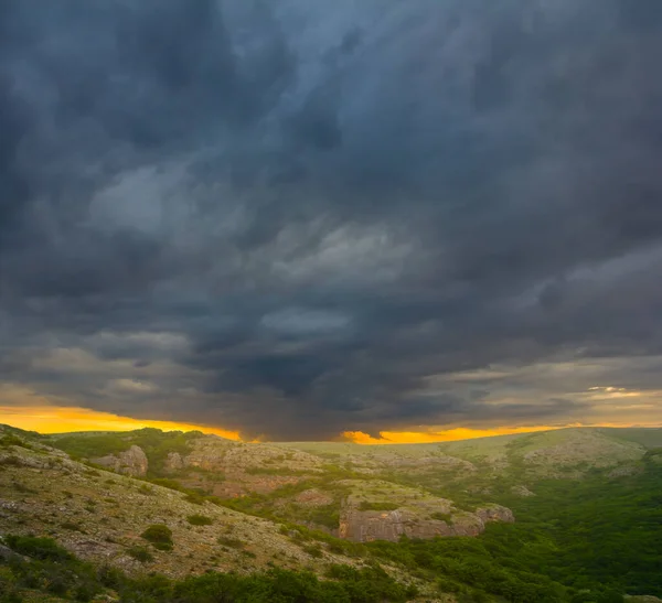 green mountain valley under dense dark cloudy sky, dramatic mountain sunset scene