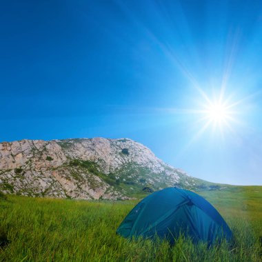 Turistik çadır, parlayan güneş ışığında dağda kalır, arka planda seyahat eder