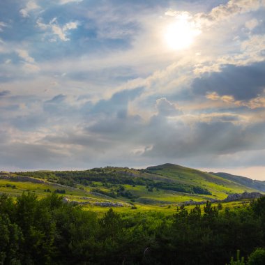 Güneşli günde bulutlu gökyüzünün altındaki yeşil dağ