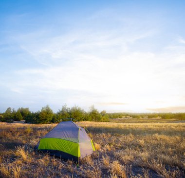 Küçük turistik çadır gün batımında bozkır arasında kalır.