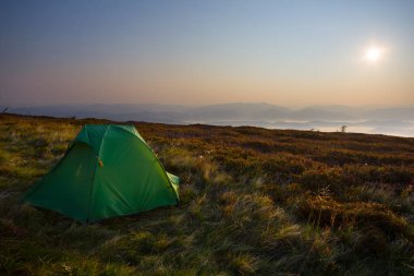 Küçük yeşil turistik çadır sabahın erken saatlerinde yamaçta kalır, doğal seyahat sahnesi.