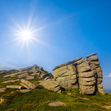 Pırıl pırıl bir güneşin altında dağın tepesinde büyük taşlar yığını, doğal seyahat arka planı.
