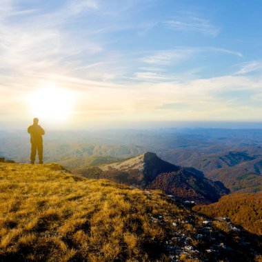 Yürüyüşçü silueti dağın tepesinde kalır ve gün batımına bakar, kavramsal seyahat sahnesi