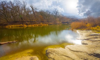 Sonbahar güneşli bir günde mavi bulutlu gökyüzünün altında ormanlı sakin bir nehir.