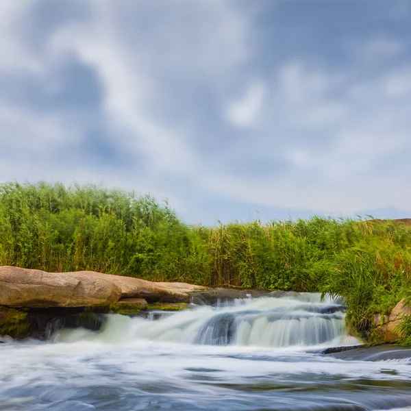 Nehir, parlak bir yaz gününde büyük bir taşın üzerinden akıyor.