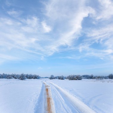 Karla kaplı kışın ortasında yol mavi bulutlu bir gökyüzünün altında
