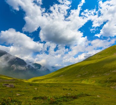 Mavi bulutlu gökyüzünün altında kar altında yeşil dağ sırtı, dağ yolculuğu sahnesi