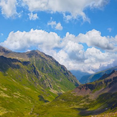 Mavi bulutlu gökyüzünün altında kar altında yeşil dağ sırtı, dağ yolculuğu sahnesi