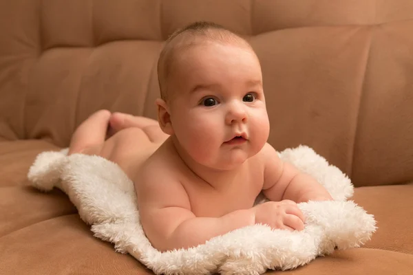 Bébé couché sur fourrure blanche, fond beige — Photo