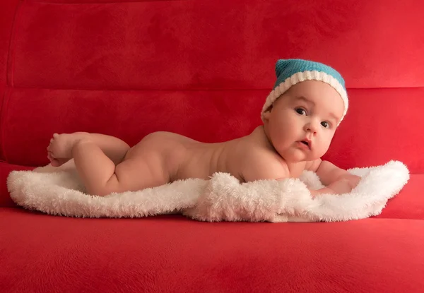 Baby in a blue cap, lying on a white skin — Stock Photo, Image