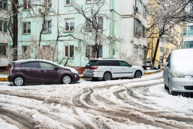 Vladivostok, Rusya - 19 Kasım 2020: ıslak karlı bir yoldaki arabaların tekerleklerinden izler. Araba buzla, karla ve buz saçaklarıyla kaplı. Kışın şehir. Buz fırtınası.