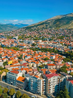 Bosna-Hersek 'in Mostar kentinin panoramik hava görüntüsü Barış Çanı Kulesi' nden alındı. Kırmızı çatıları, tarihi binaları ve açık mavi gökyüzünün altındaki dağları olan güzel bir şehir.