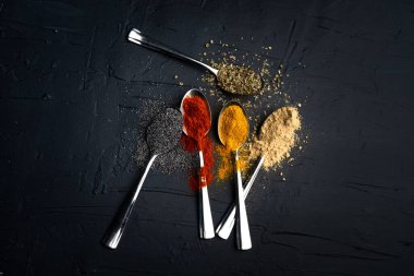 Siyah arka planda metal kaşıkta baharatlar