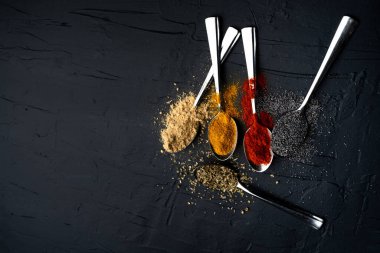 Siyah arka planda metal kaşıkta baharatlar