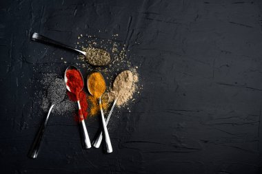 Siyah arka planda metal kaşıkta baharatlar