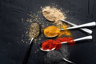 Siyah arka planda metal kaşıkta baharatlar