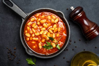 Siyah zemin üzerine dökme demir tavada fırınlanmış fasulye yemeği..