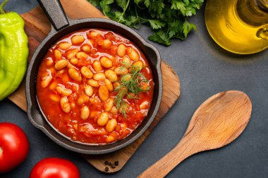 Siyah zemin üzerine dökme demir tavada fırınlanmış fasulye yemeği..