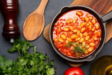 Siyah zemin üzerine dökme demir tavada fırınlanmış fasulye yemeği..