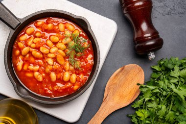 Siyah zemin üzerine dökme demir tavada fırınlanmış fasulye yemeği..