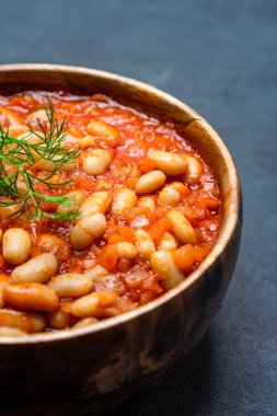 Siyah arka planda, ahşap kasede pişirilmiş fasulye yemeği..