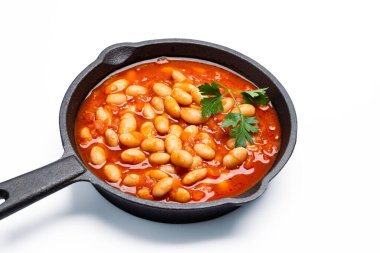 Beyaz zemin üzerinde dökme demir tavada fırınlanmış fasulye yemeği.