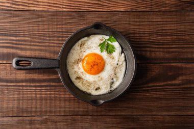 Bir yumurta ahşap arka planda dökme demir bir tavada pişiyor.