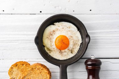 Beyaz ahşap arka planda dökme demir bir tavada pişirilmiş bir yumurta.