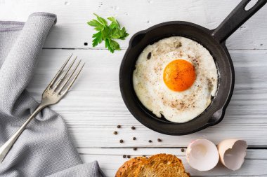 One egg cooked in a cast iron pan on white wooden background