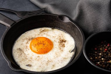 Bir yumurta, siyah taş arka planda dökme demir bir tavada pişiyor.