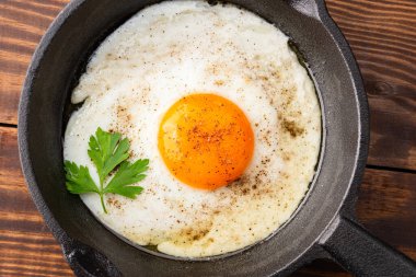 Bir yumurta ahşap arka planda dökme demir bir tavada pişiyor.