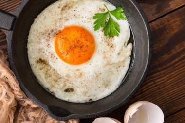 Bir yumurta ahşap arka planda dökme demir bir tavada pişiyor.