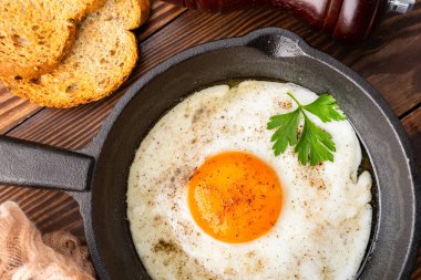 Bir yumurta ahşap arka planda dökme demir bir tavada pişiyor.