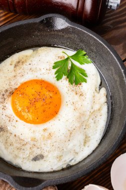 Bir yumurta ahşap arka planda dökme demir bir tavada pişiyor.