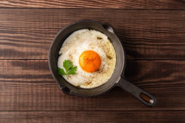 Bir yumurta ahşap arka planda dökme demir bir tavada pişiyor.