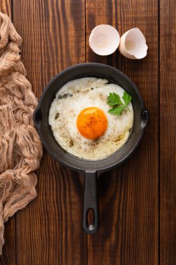 Bir yumurta ahşap arka planda dökme demir bir tavada pişiyor.
