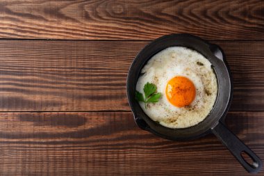 Bir yumurta ahşap arka planda dökme demir bir tavada pişiyor.