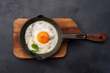 Bir yumurta, siyah taş arka planda dökme demir bir tavada pişiyor.
