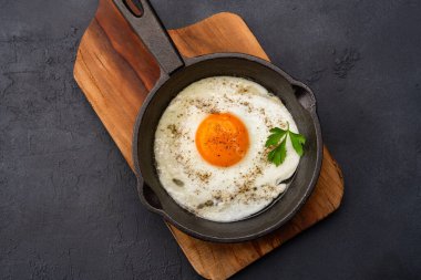 Bir yumurta, siyah taş arka planda dökme demir bir tavada pişiyor.