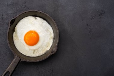 Bir yumurta, siyah taş arka planda dökme demir bir tavada pişiyor.
