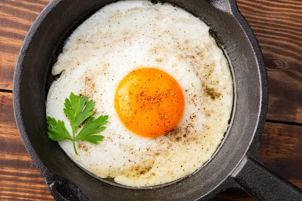 Bir yumurta ahşap arka planda dökme demir bir tavada pişiyor.