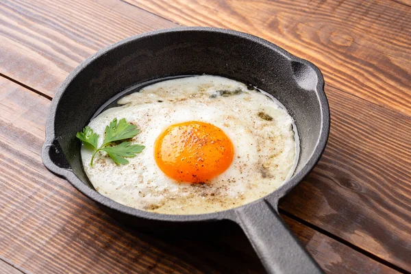 Bir yumurta ahşap arka planda dökme demir bir tavada pişiyor.