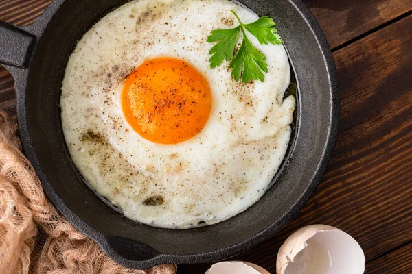 Bir yumurta ahşap arka planda dökme demir bir tavada pişiyor.