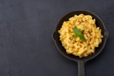 Siyah taş arka planda lezzetli bir tavada peynirli makarna.