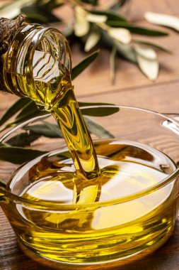 Sürahiden ahşap masada cam kaseye organik zeytin yağı dökülüyor.