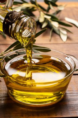 Sürahiden ahşap masada cam kaseye organik zeytin yağı dökülüyor.
